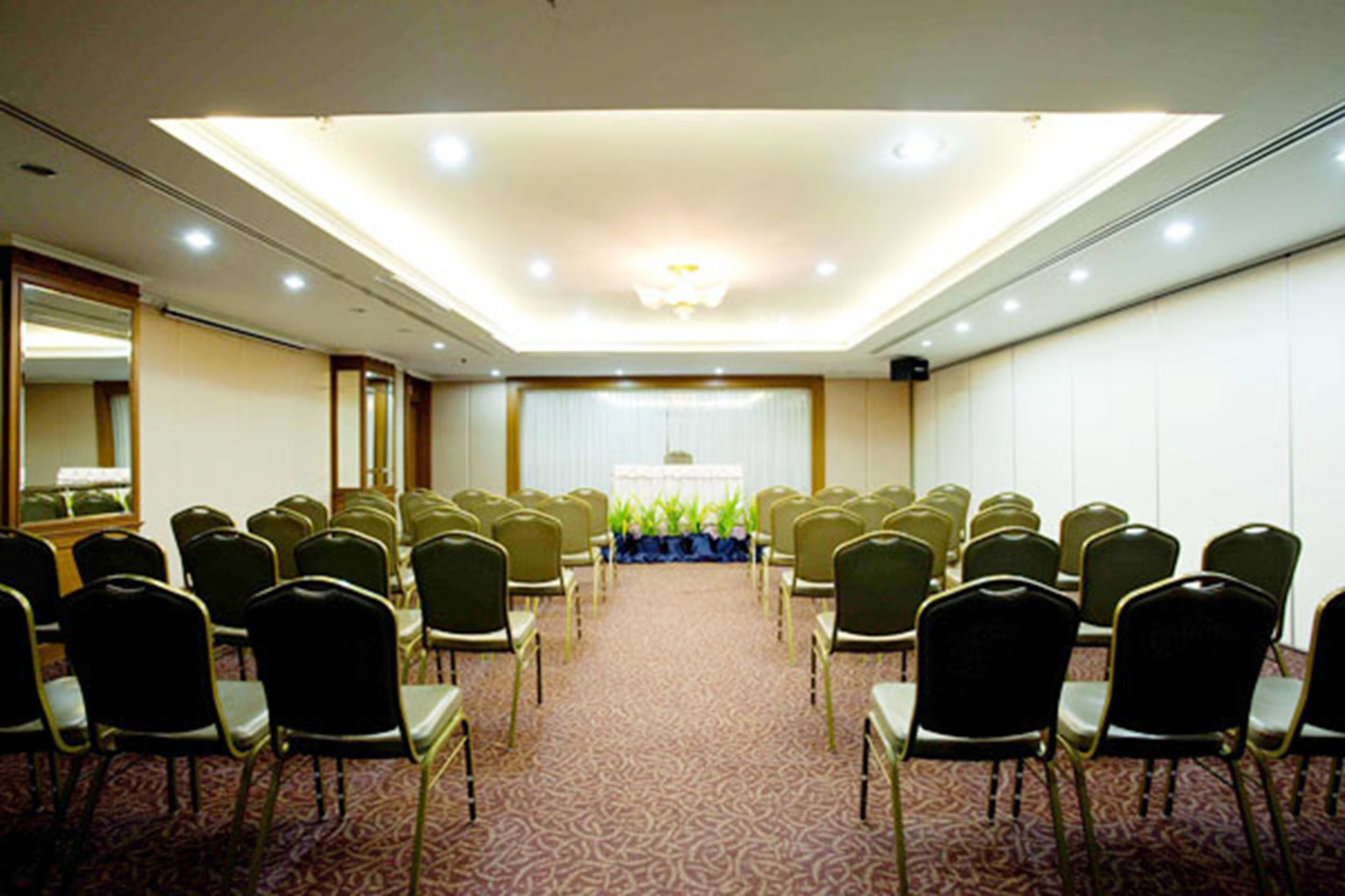 A conference room with rows of chairs facing a stage, a carpeted floor, and a ceiling with recessed lighting.