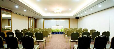 A conference room with rows of chairs facing a stage, a carpeted floor, and a ceiling with recessed lighting.