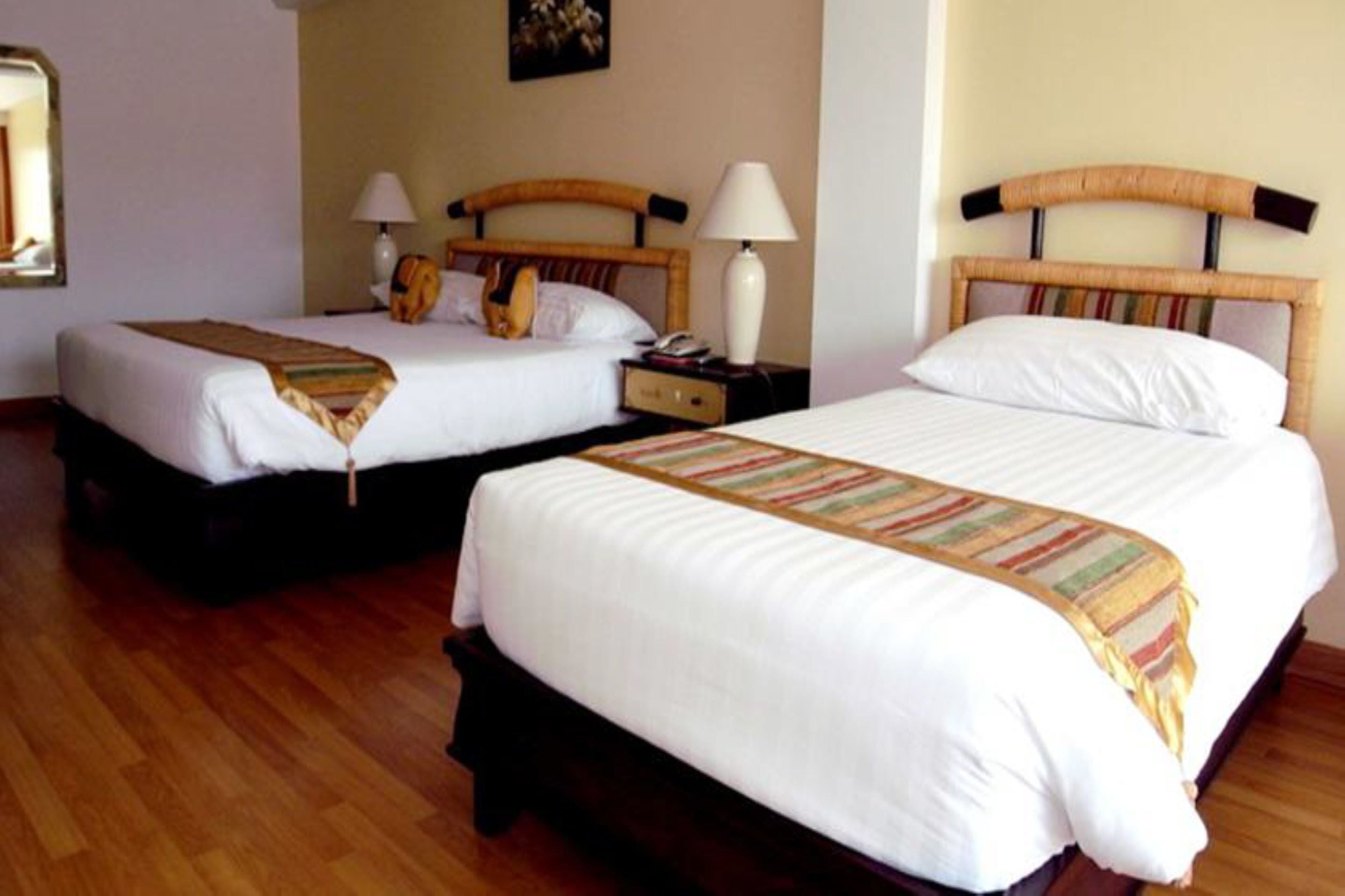 Una habitación de hotel con dos camas individuales, cabeceros de madera, ropa de cama blanca y lámparas de noche.
