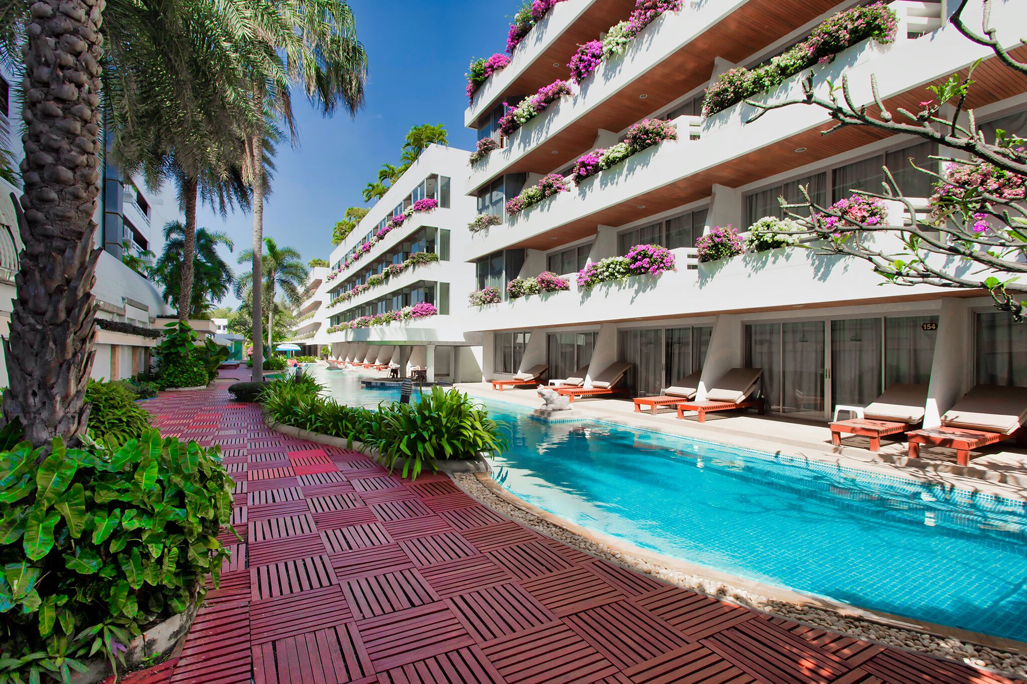 Un hotel con piscina, mobiliario exterior y balcones adornados con flores.