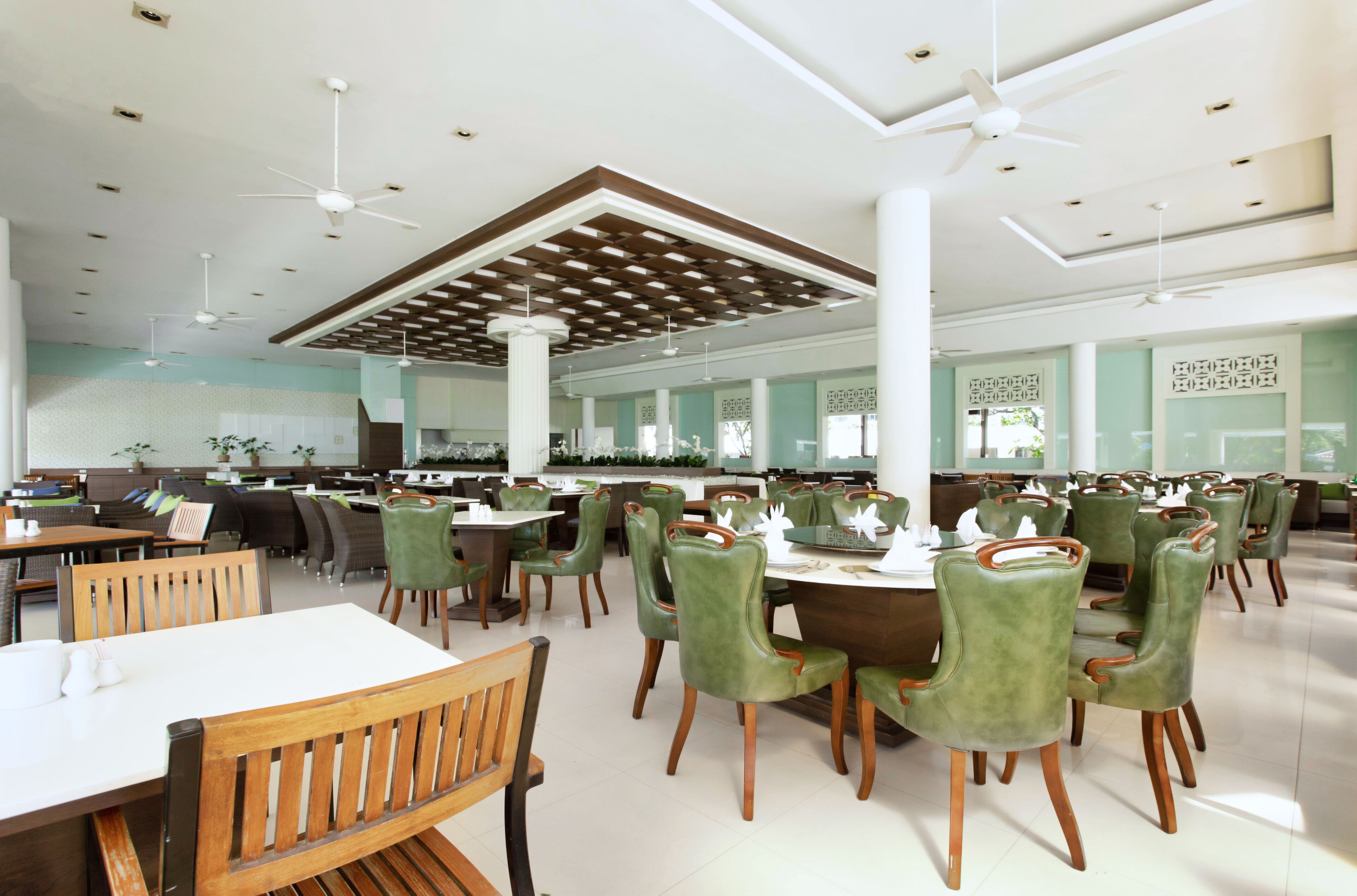 A spacious restaurant with high ceilings, multiple dining areas, and green upholstered chairs.