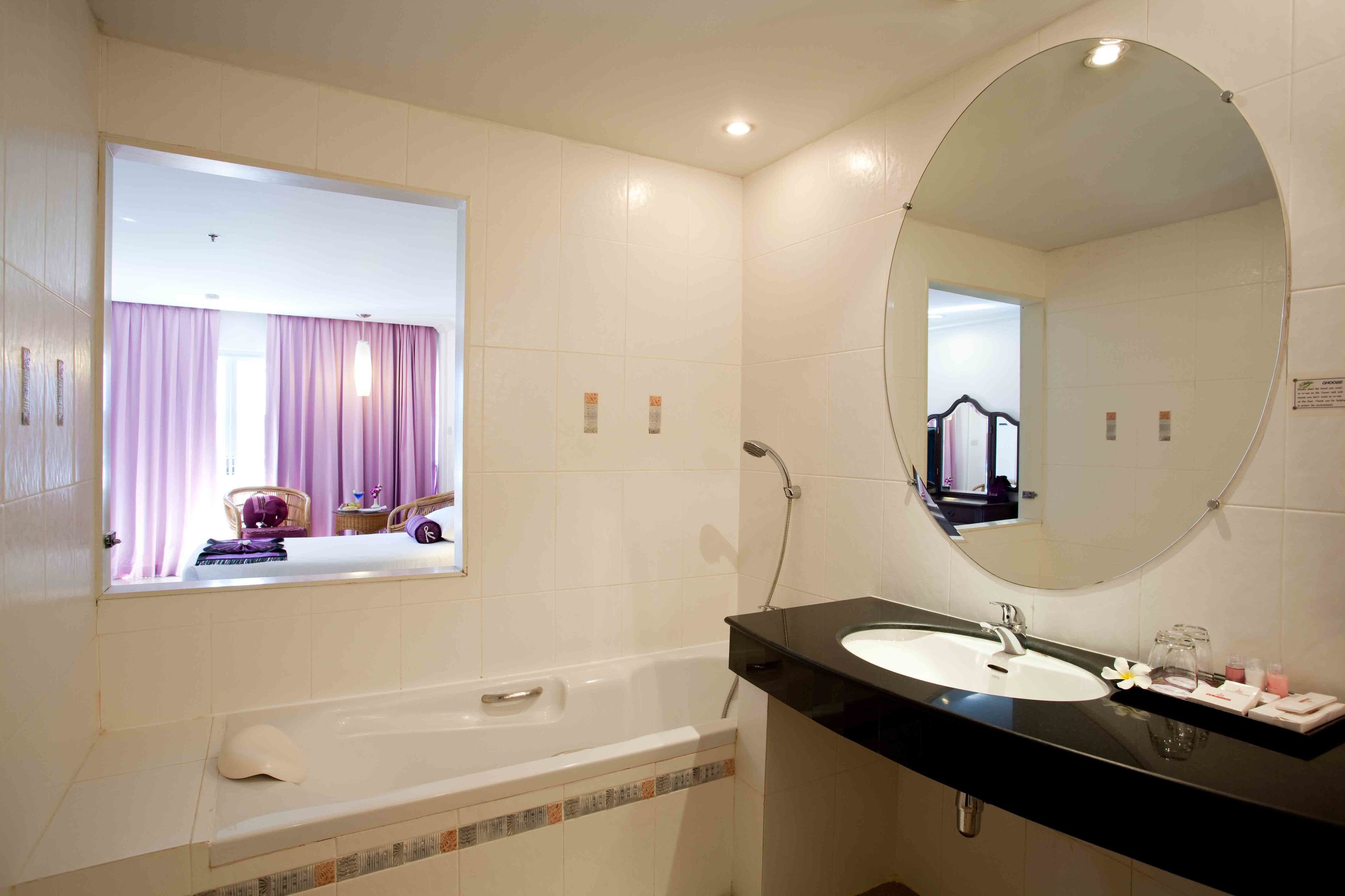 Ein Badezimmer mit Badewanne, Waschbecken, einem großen Spiegel und einem Fenster mit Vorhängen.