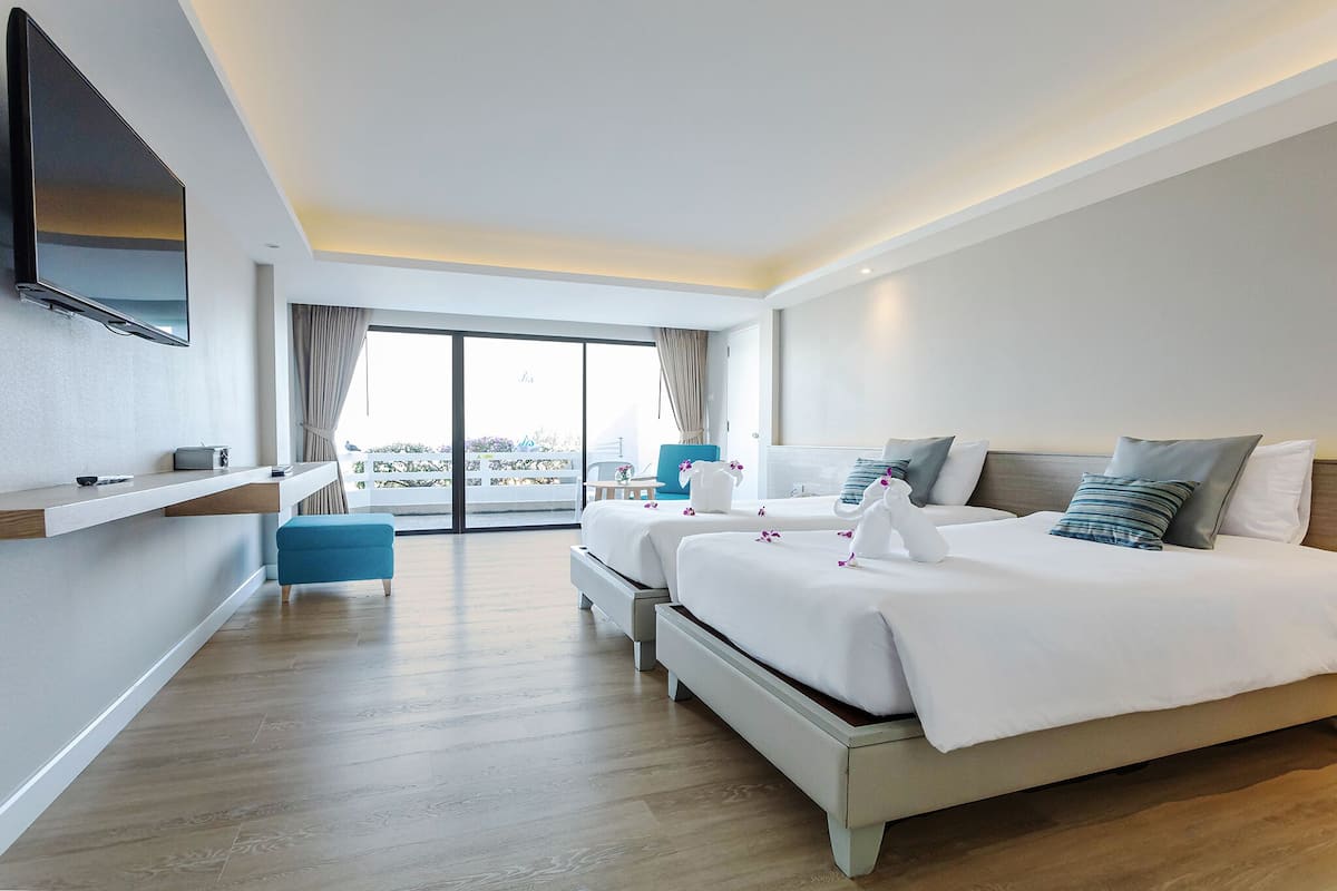 Hotelkamer met twee bedden, een aan de muur bevestigde televisie, een balkon met uitzicht en een houten vloer.