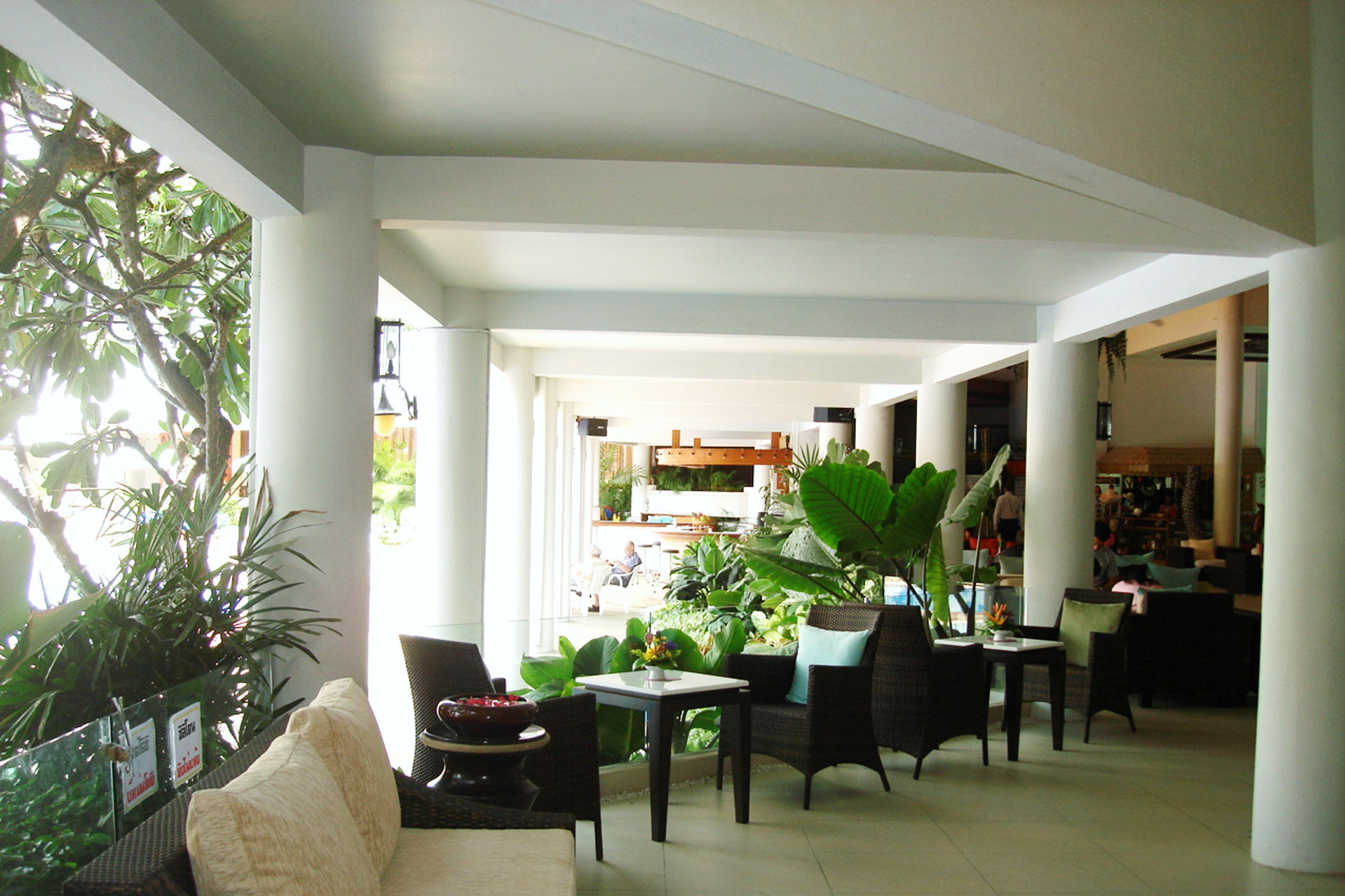 A spacious indoor area with multiple seating arrangements, including sofas and chairs, surrounded by large potted plants.