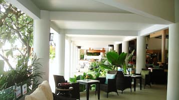 A spacious indoor area with multiple seating arrangements, including sofas and chairs, surrounded by large potted plants.