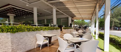 An outdoor cafe with white wicker furniture, stone walls, and a covered seating area.