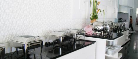 Disposición de bufé con varias estaciones de servicio, un salpicadero de azulejos blancos y una planta en maceta.