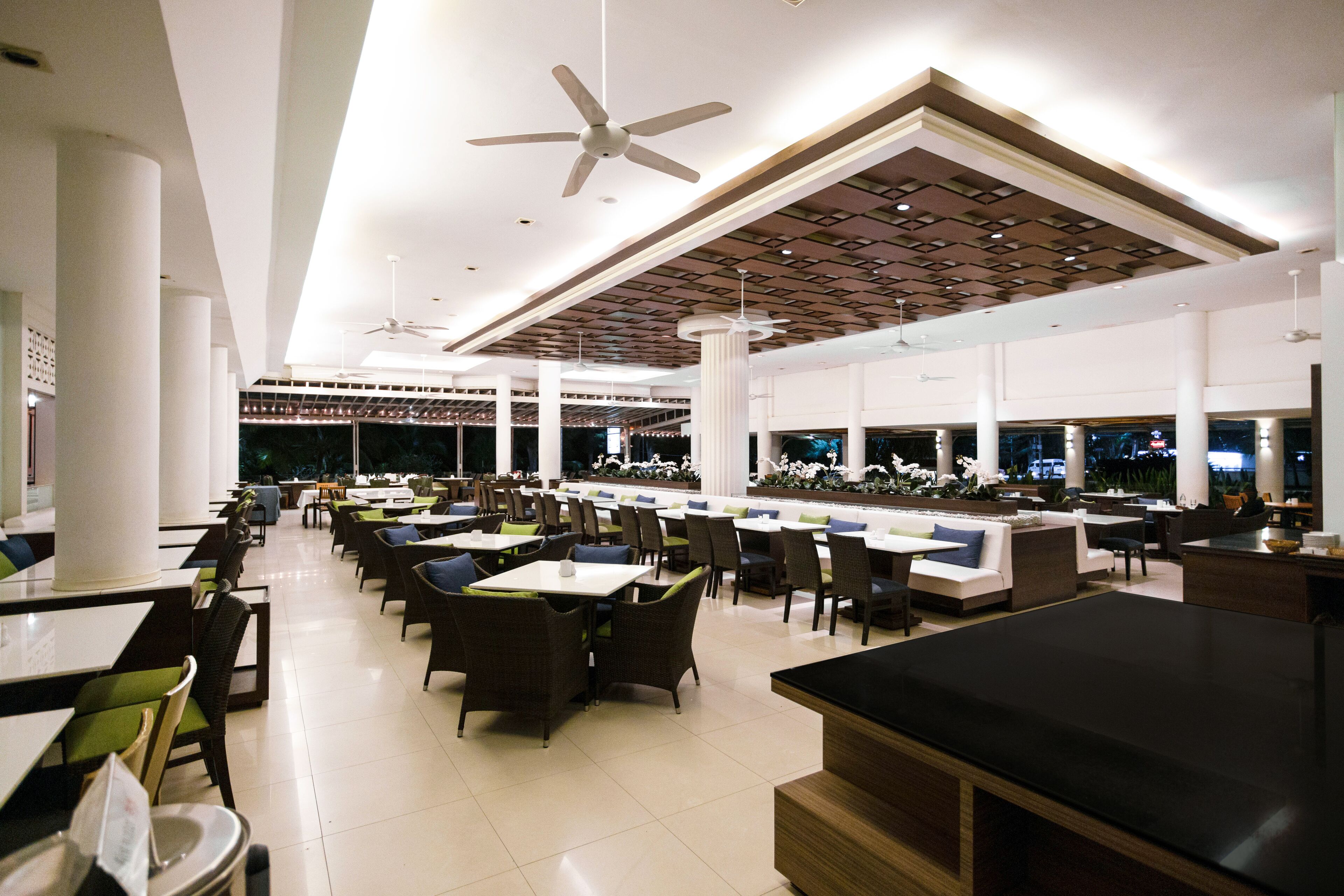 A spacious restaurant with high ceilings, modern lighting, and multiple seating areas including tables and chairs.