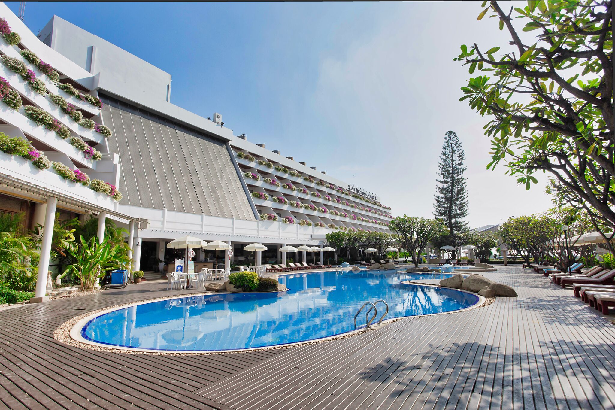 A hotel with a swimming pool, lounge chairs, and a covered area with umbrellas.