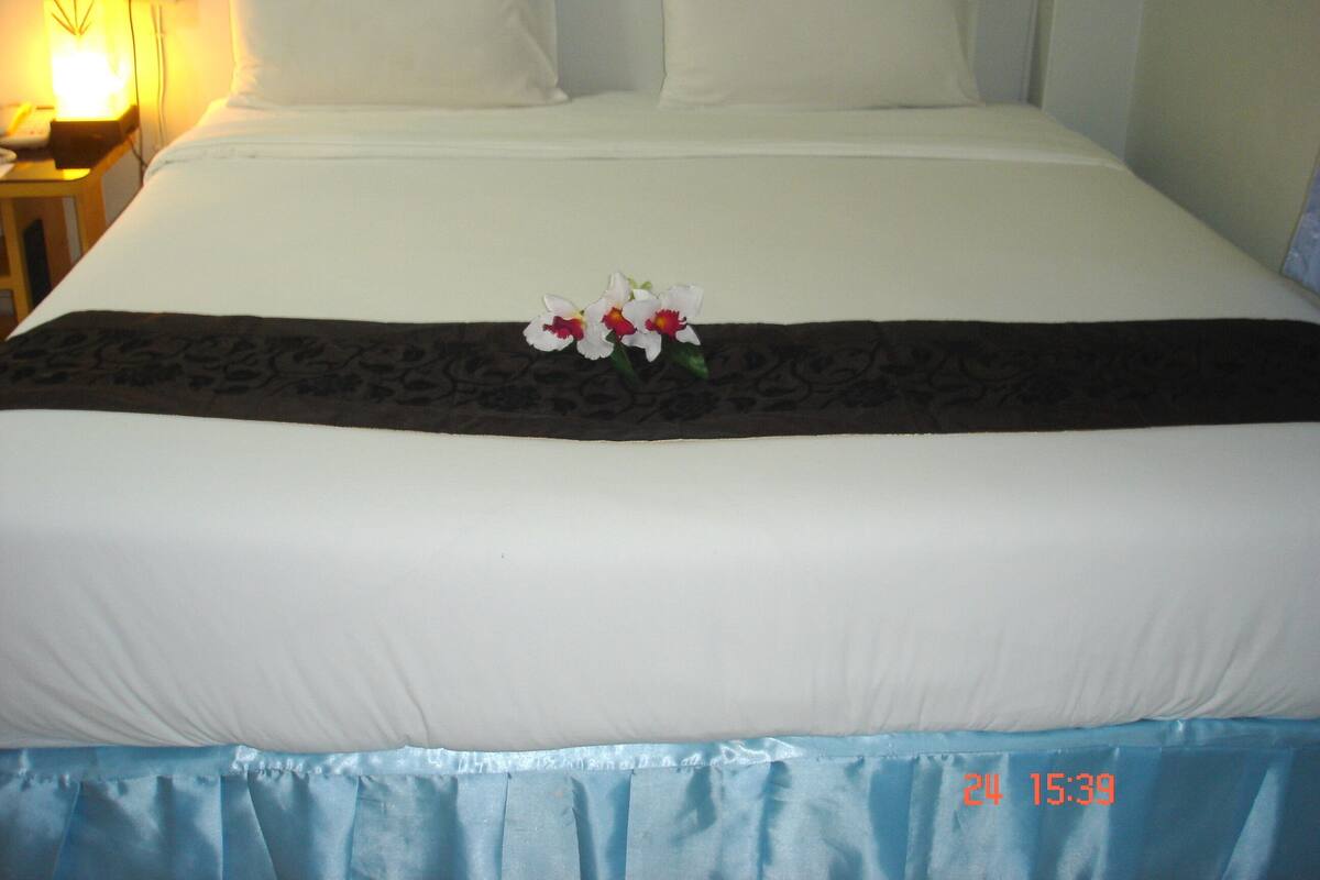 A neatly made bed with white linens, a dark brown decorative bed runner, and a pair of white pillows.