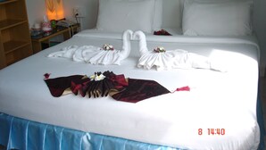 A hotel room with a neatly made bed featuring a swan towel design and a bouquet of flowers. - Lamai Apartment (Patong)