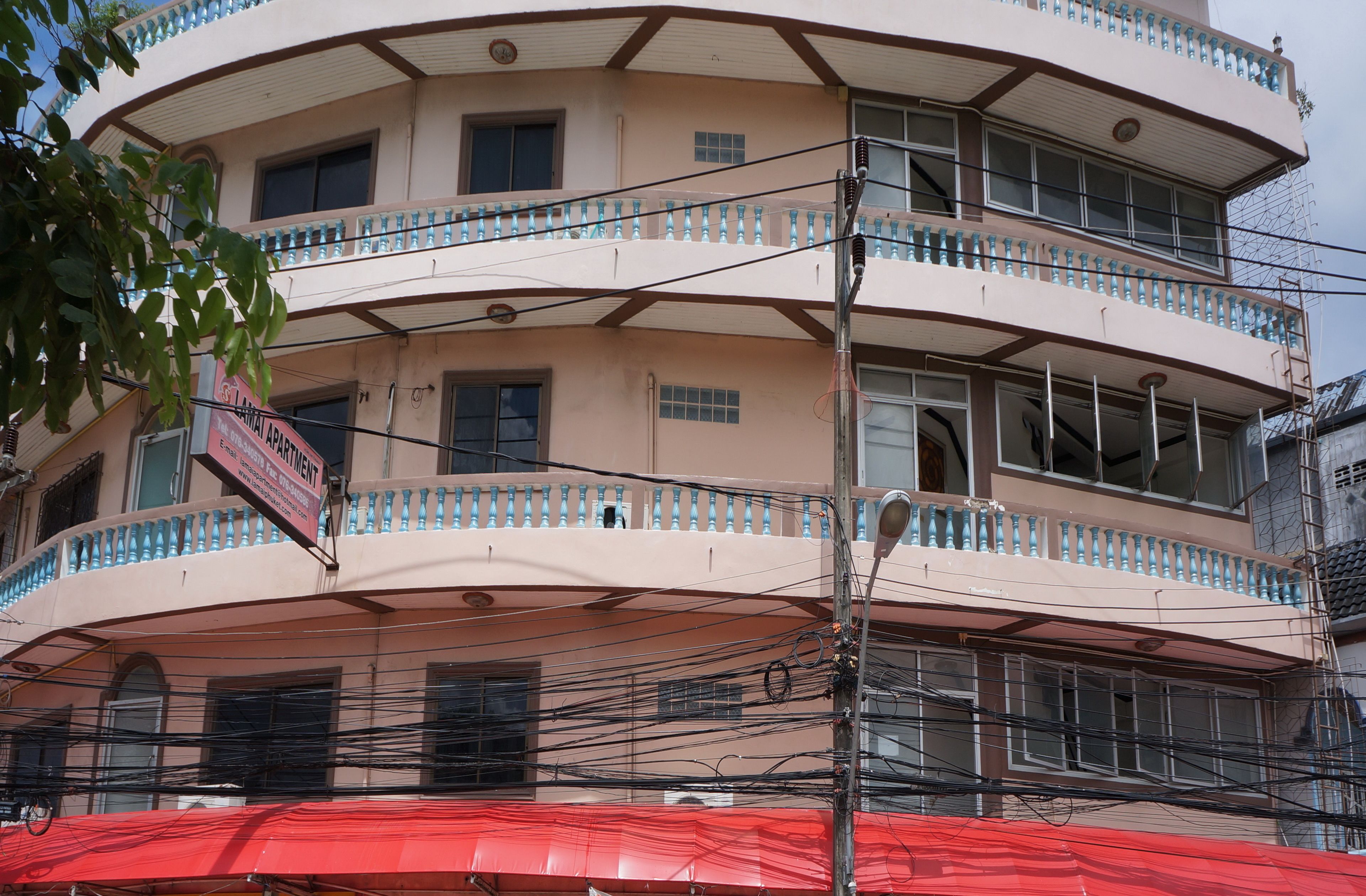 A multi-story building with balconies, a sign indicating it is an apartment building, and numerous electrical wires.