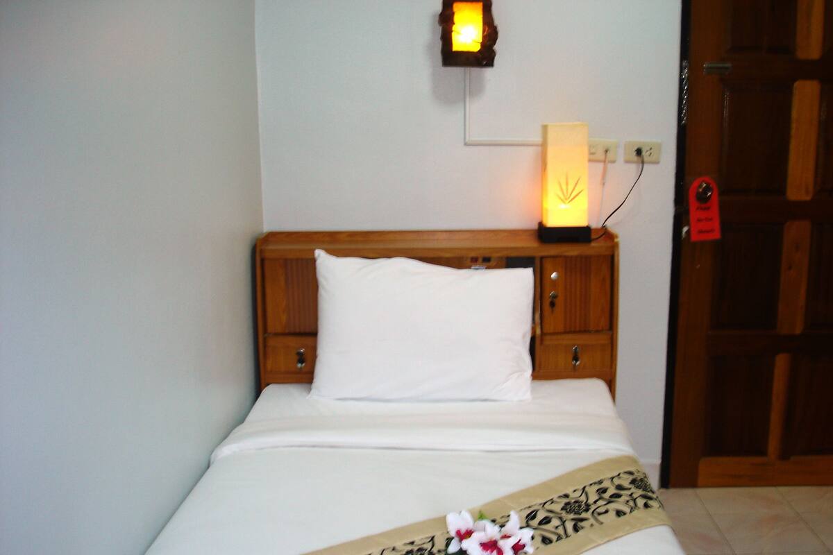 A neatly made bed with a white pillow and a decorative pillow with a floral pattern. A wall-mounted light fixture is visible above the bed.