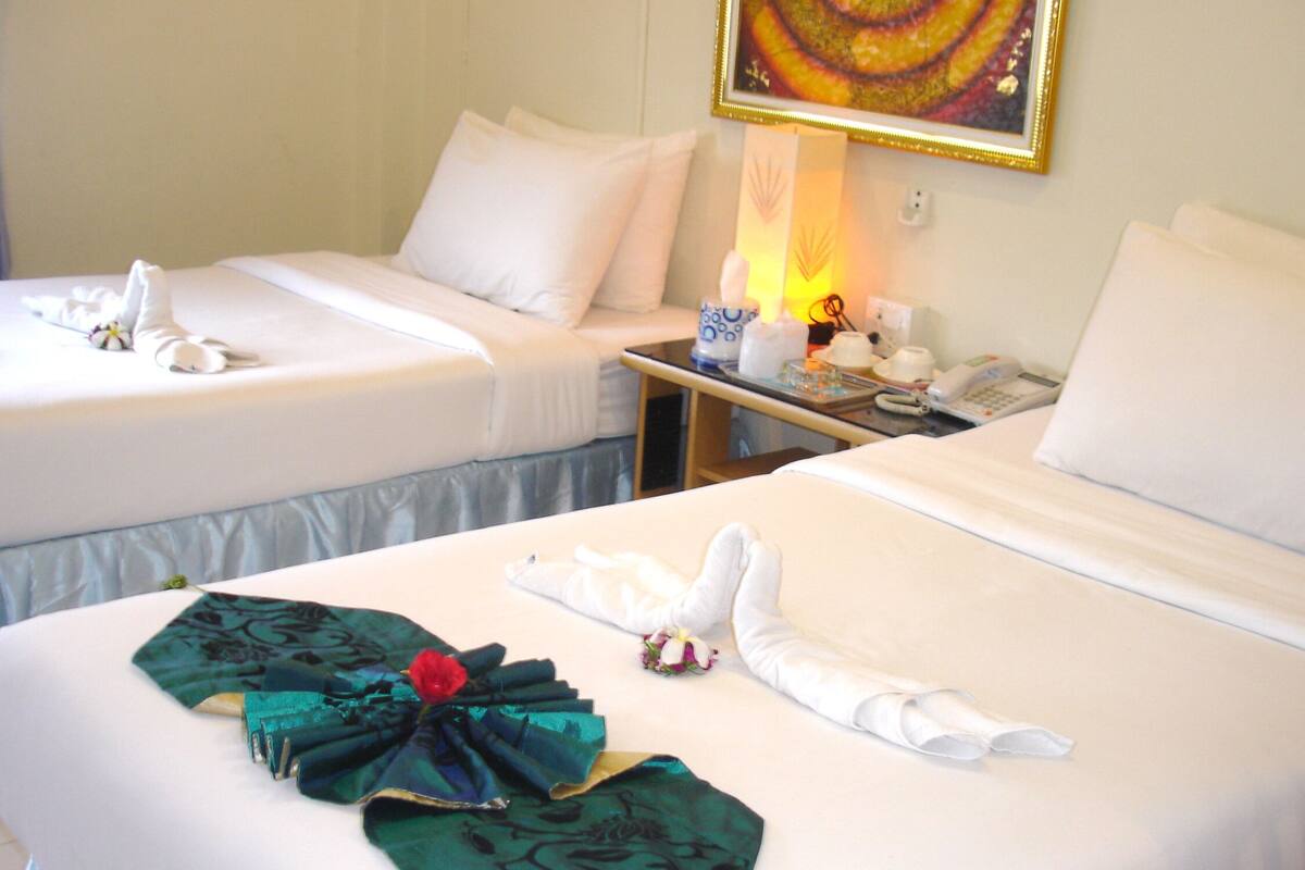 Two neatly made beds with white linens, a bedside table with a lamp, a phone, and a painting on the wall.