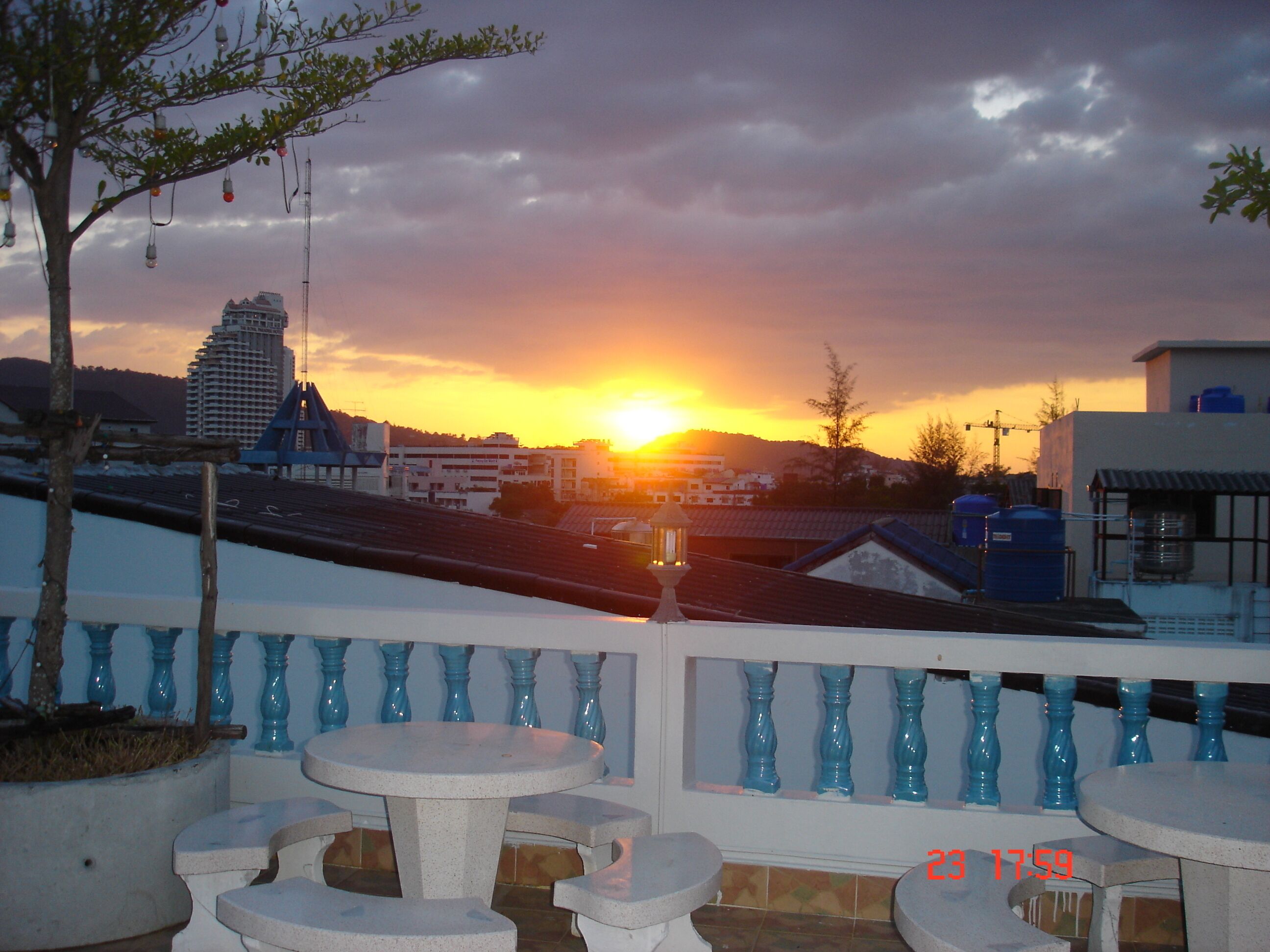 Una terrazza con vista su un tramonto sopra una città, con ringhiera caratterizzata da dettagli blu e tavolo con sedie.