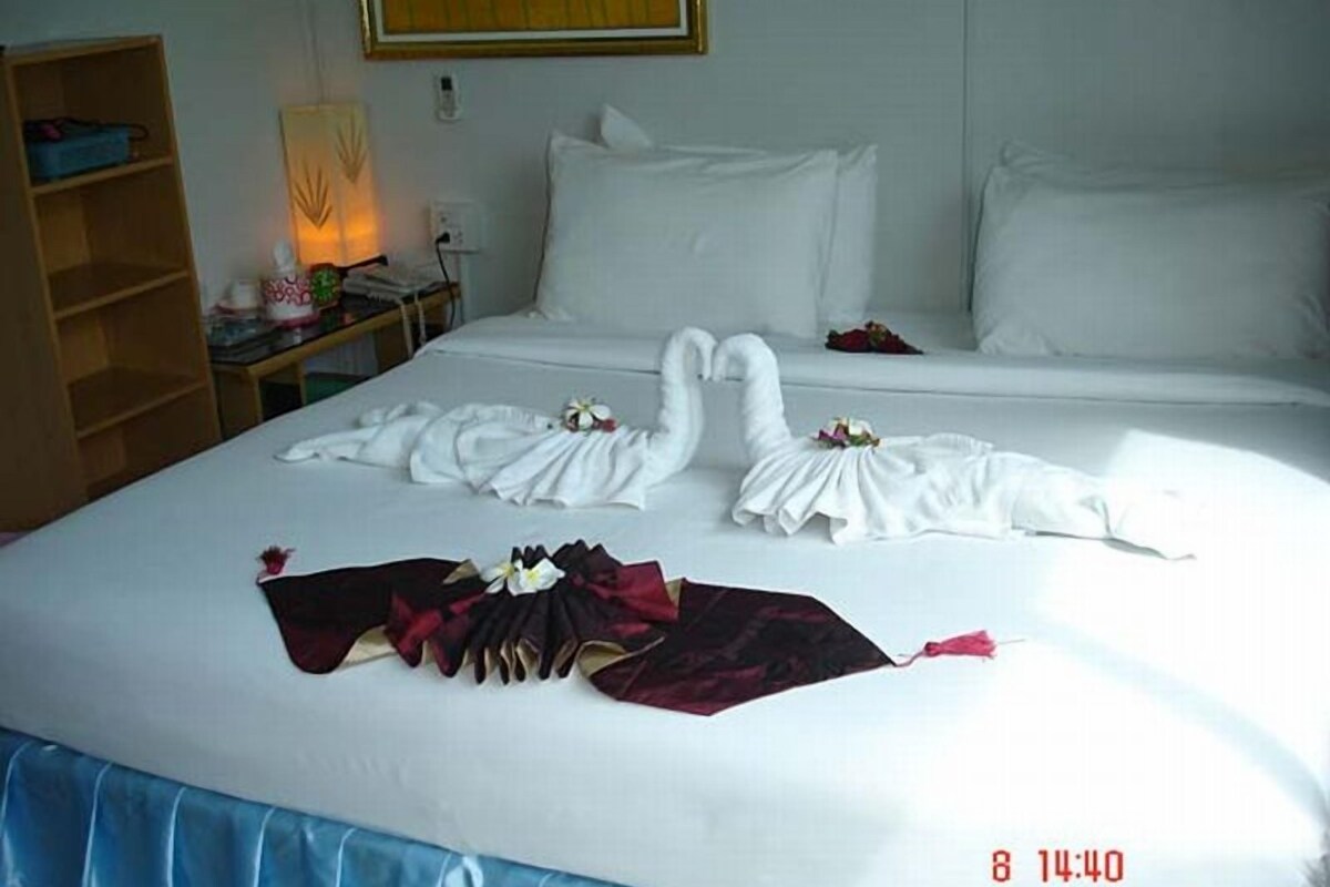 Ein Hotelzimmer mit einem ordentlich bezogenen Bett, einem Nachttisch mit Lampe und einer Holzablage.
