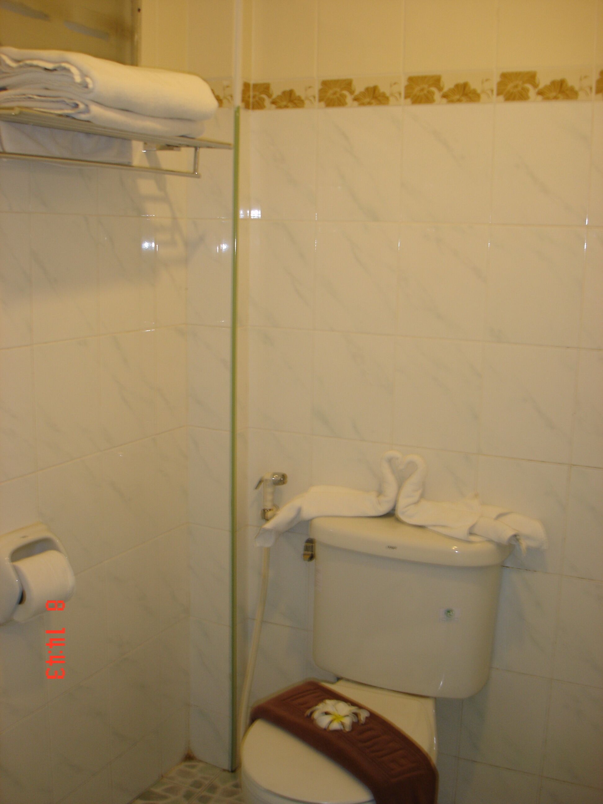 A bathroom with a toilet, a towel rack with folded towels, and a toilet paper dispenser.