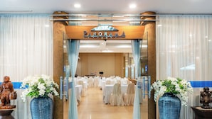 A restaurant entrance with a sign reading "PANORAMA RESTAURANT," large blue vases with white flowers, and a banquet hall in the background.