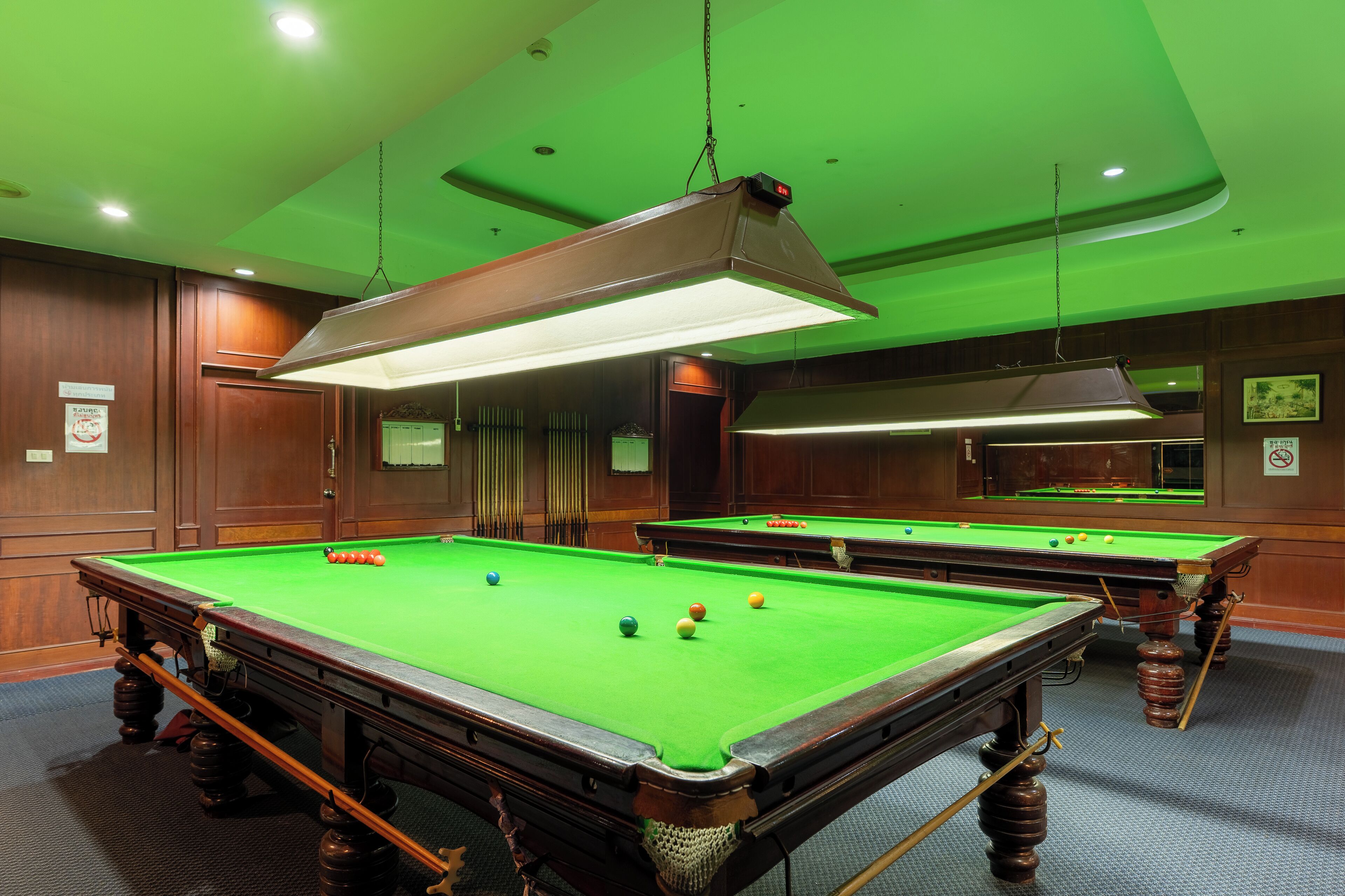 Uma mesa de bilhar com bolas, superfície em feltro verde e iluminação pendente.