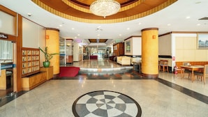 A hotel lobby with a central chandelier, a reception desk, a seating area, and a fire extinguisher.