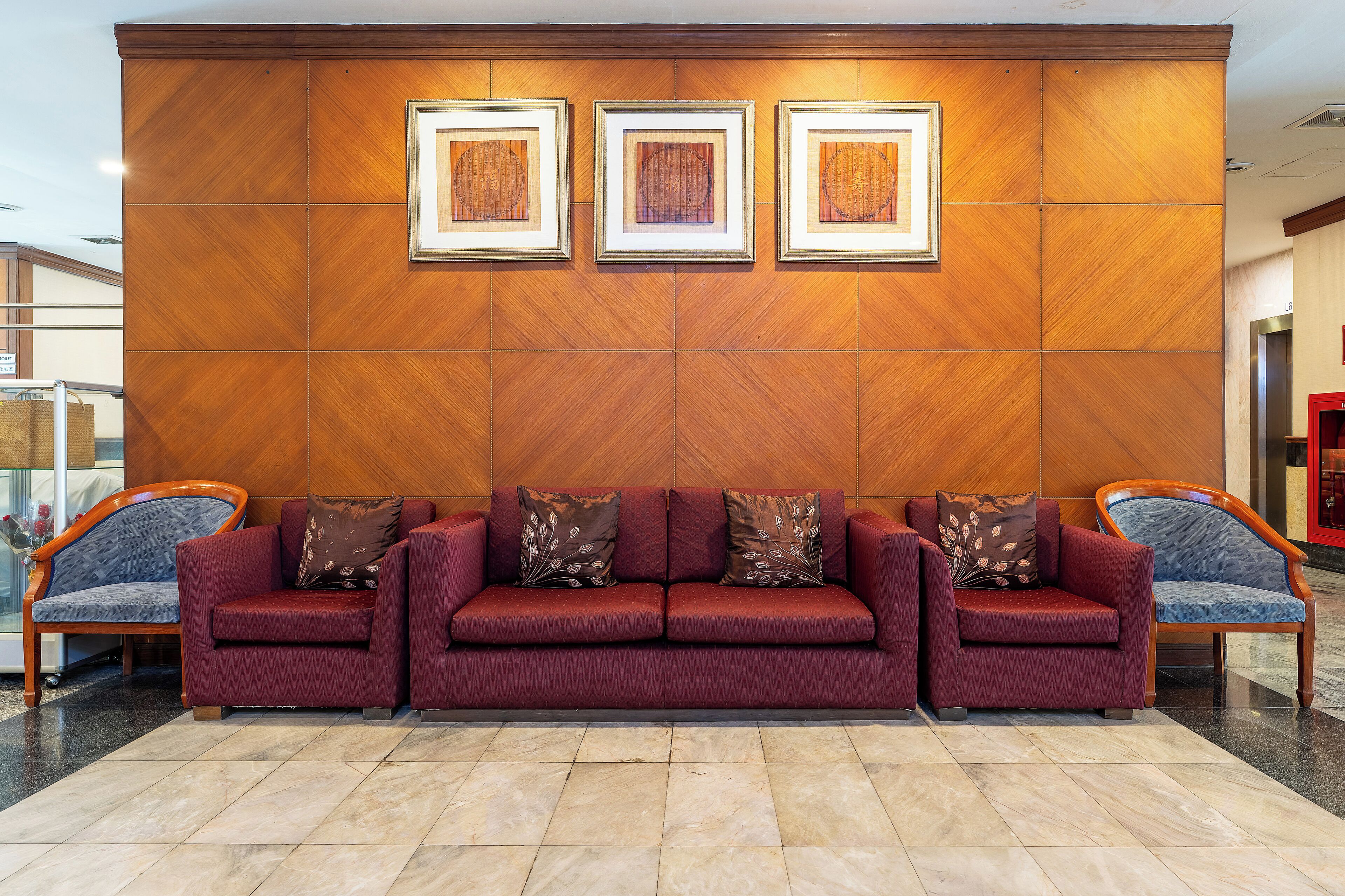A reception area with a red sofa, two armchairs, and a wooden wall with framed artwork.