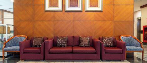 A reception area with a red sofa, two armchairs, and a wooden wall with framed artwork.