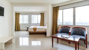 A hotel room with a bed, a desk, two chairs, a TV, and large windows with curtains.