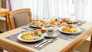 A breakfast table set with plates of food, a cup of coffee, and a glass of orange juice.