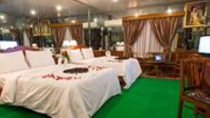A hotel room with a large bed, a desk, and a chair. There is a green carpet and curtains on the windows. - Asia Hotel (Phnom Penh)