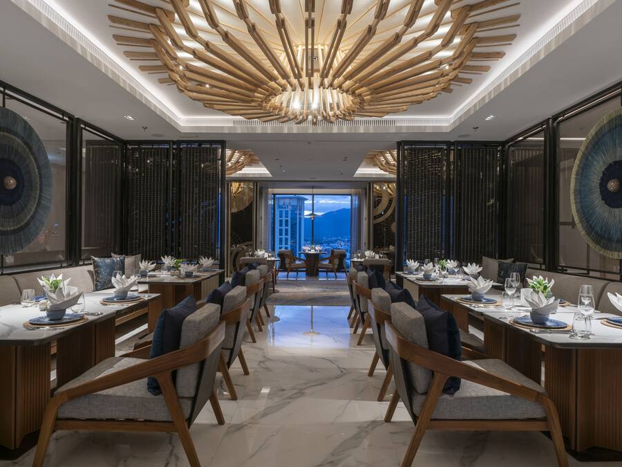 A modern dining area with a central table and chairs, a unique ceiling design, and a view through a glass door.