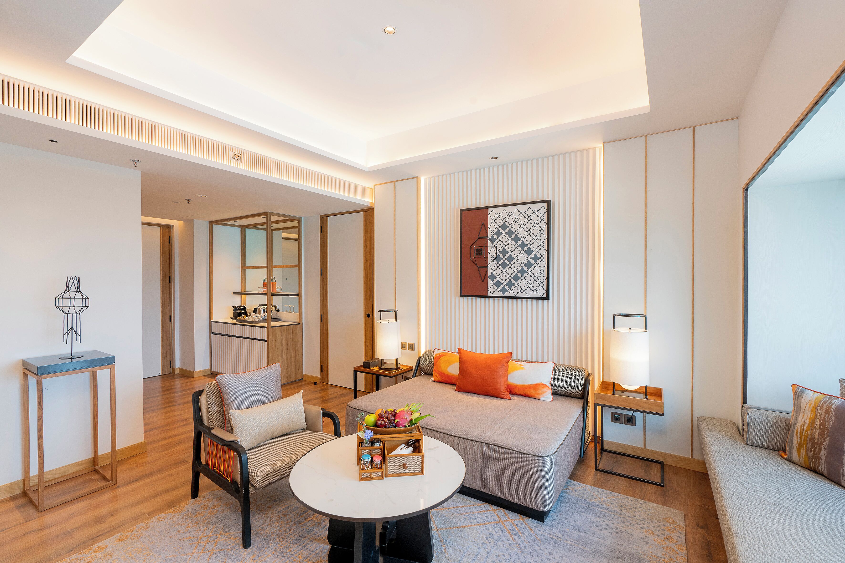 A modern hotel room with a bed, sofa, round table, and a small kitchen area.