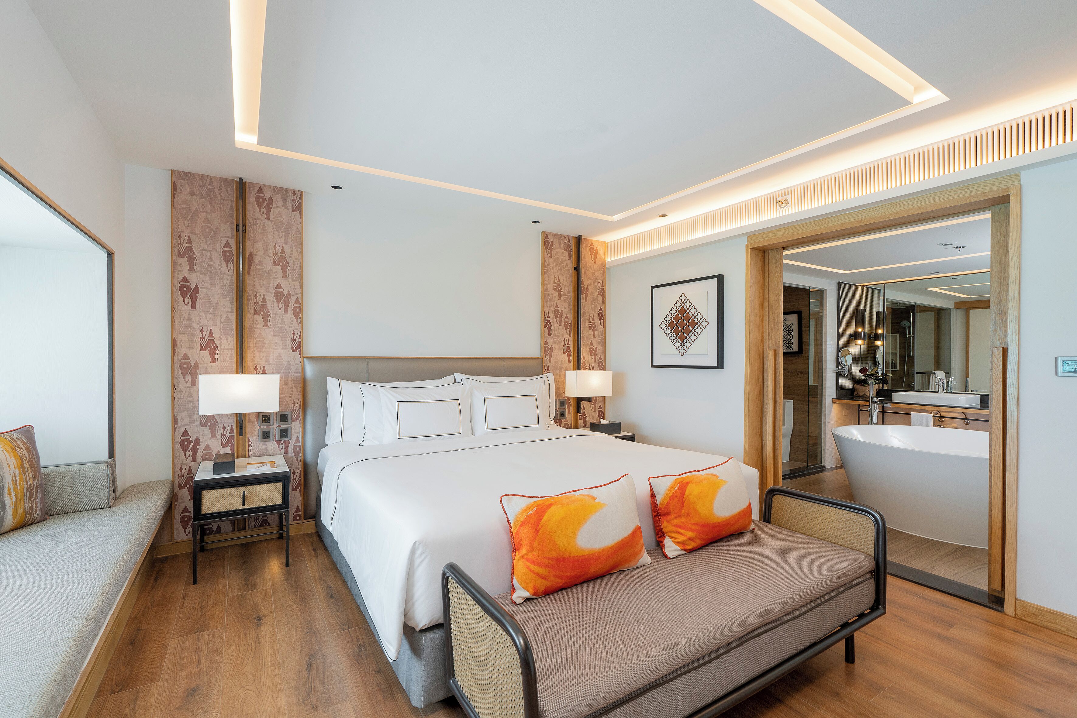 A modern hotel room with a large bed, bedside tables, a sofa, a bathroom with a bathtub, and a large mirror.