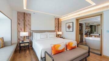 A modern hotel room with a large bed, bedside tables, a sofa, a bathroom with a bathtub, and a large mirror.