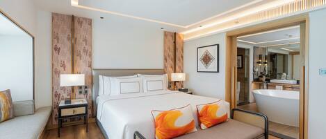 A modern hotel room with a large bed, bedside tables, a sofa, a bathroom with a bathtub, and a large mirror.