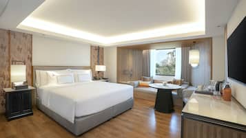 A modern hotel room with a large bed, a sofa, a dining table, and a TV.
