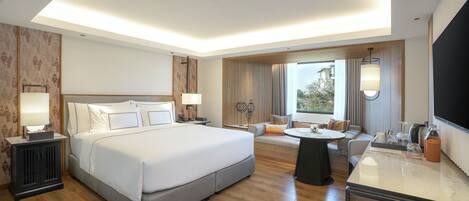A modern hotel room with a large bed, a sofa, a dining table, and a TV.
