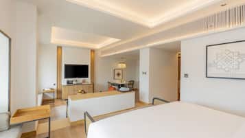A modern hotel room with a large bed, a desk, a flat-screen TV, and a dining area.