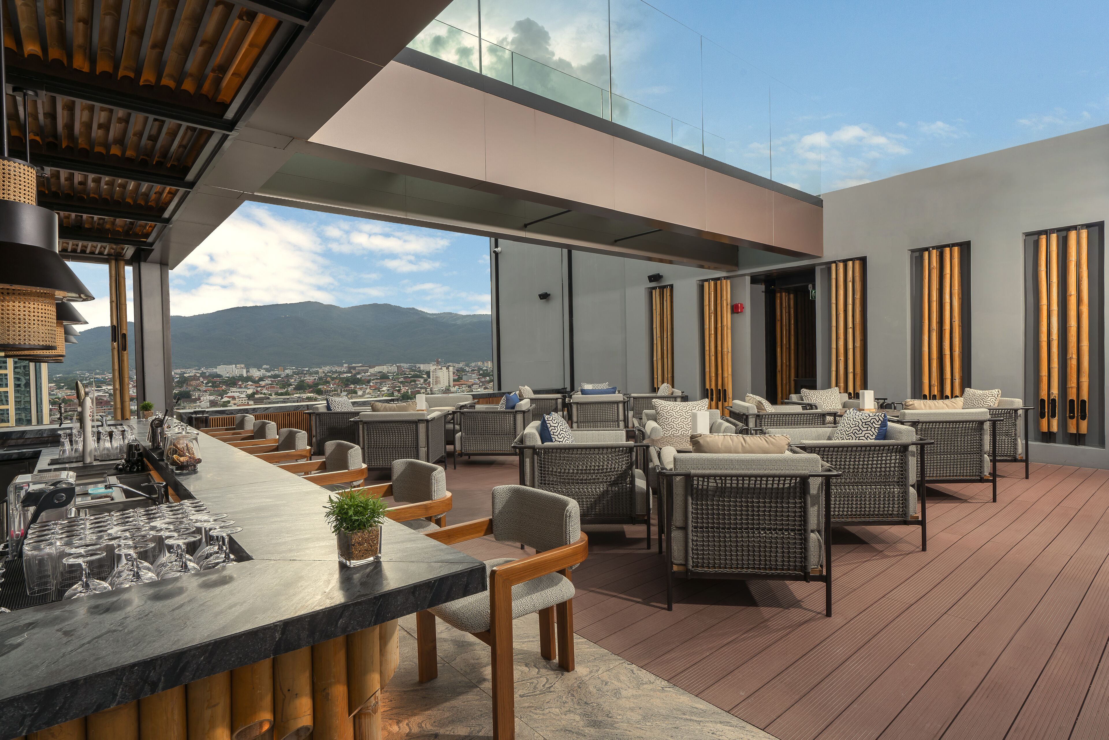 A rooftop bar with wicker furniture, a bar counter, and a view of the city and mountains.