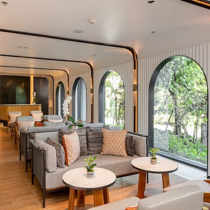 A modern interior with a sofa, two round tables, and a view of greenery through large windows.