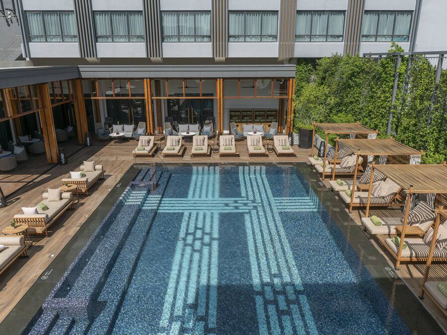 A rooftop pool area with lounge chairs and umbrellas, surrounded by a modern building with large windows.
