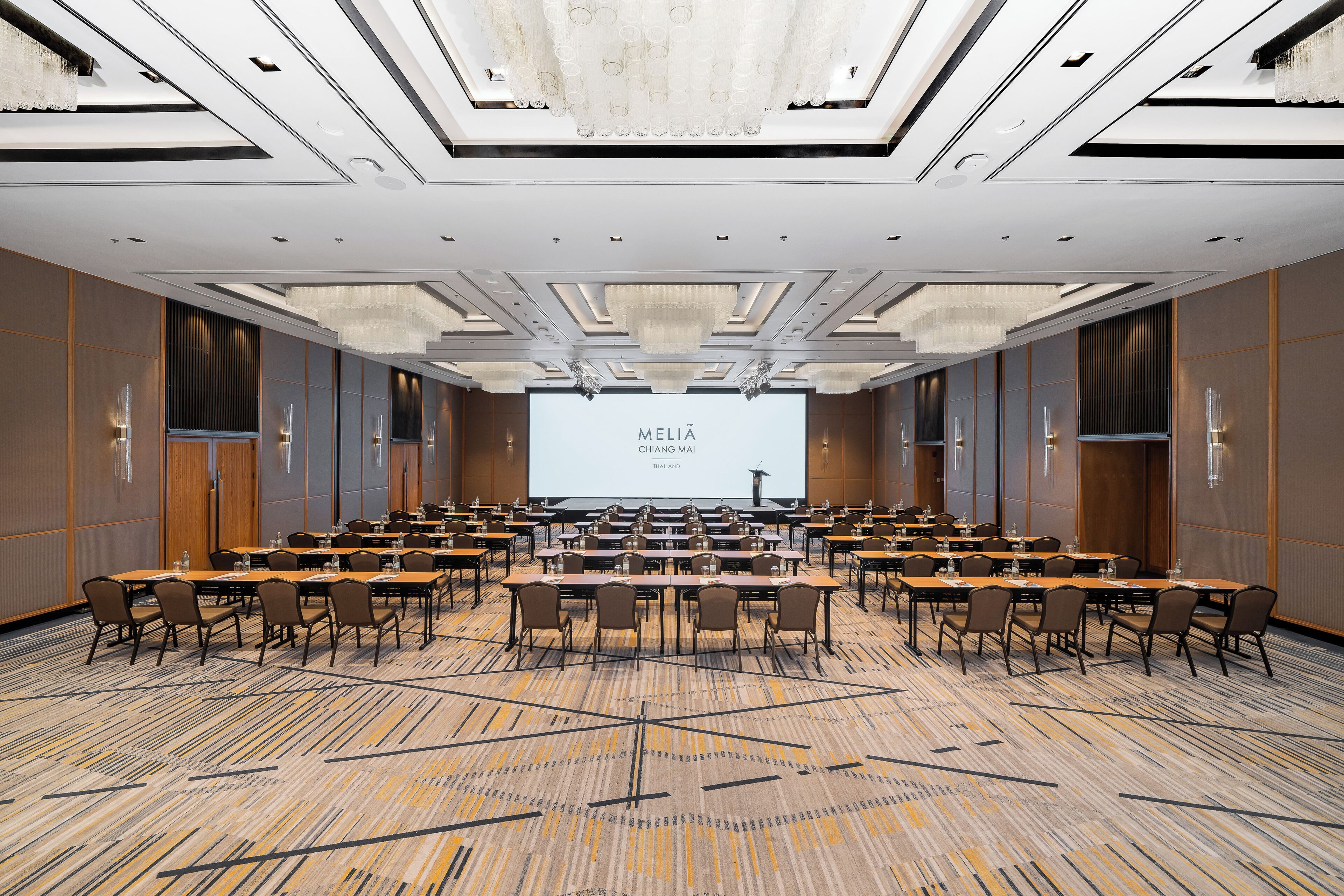 A conference room with a large screen displaying 'MELIA CHANG MAI' and a presentation. The room has multiple tables and chairs arranged for meetings.