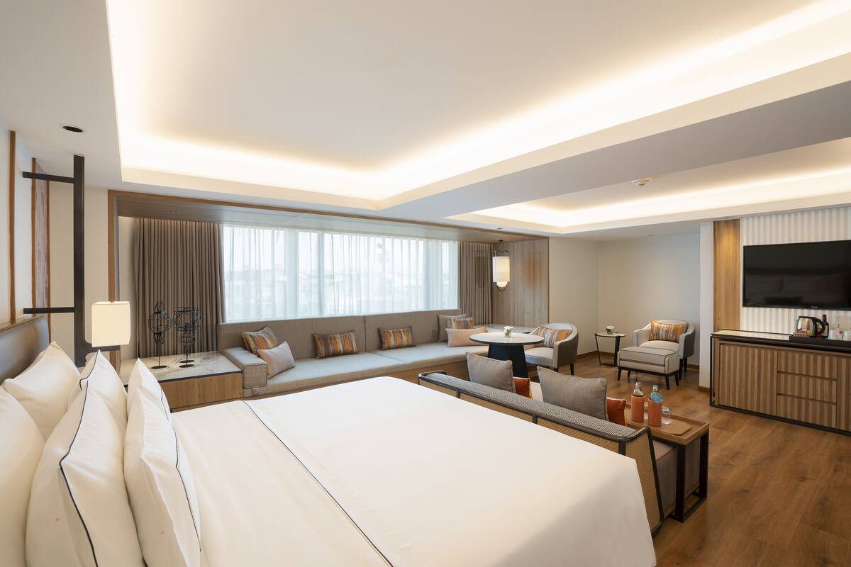 Ein modernes Hotelzimmer mit einem großen Bett, einer Couch, einem Essbereich und einem Fernseher.
