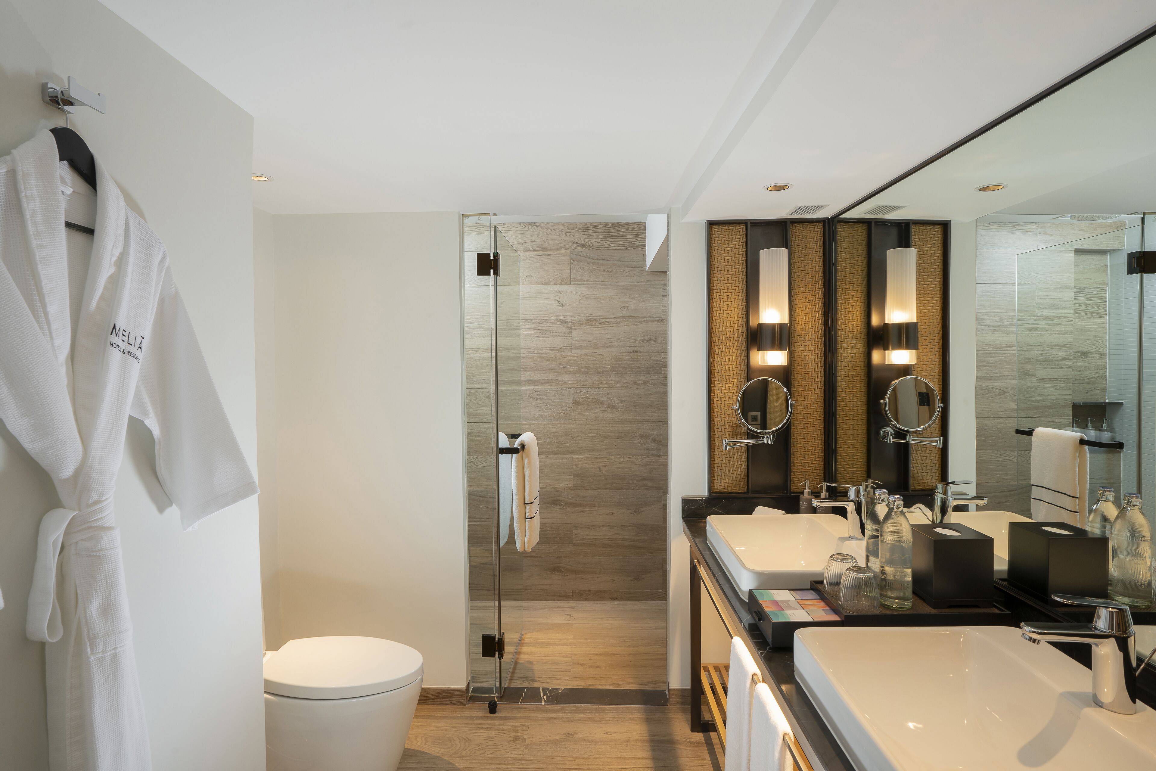 Un baño moderno con cabina de ducha de vidrio, dos lavamanos y un espejo grande.
