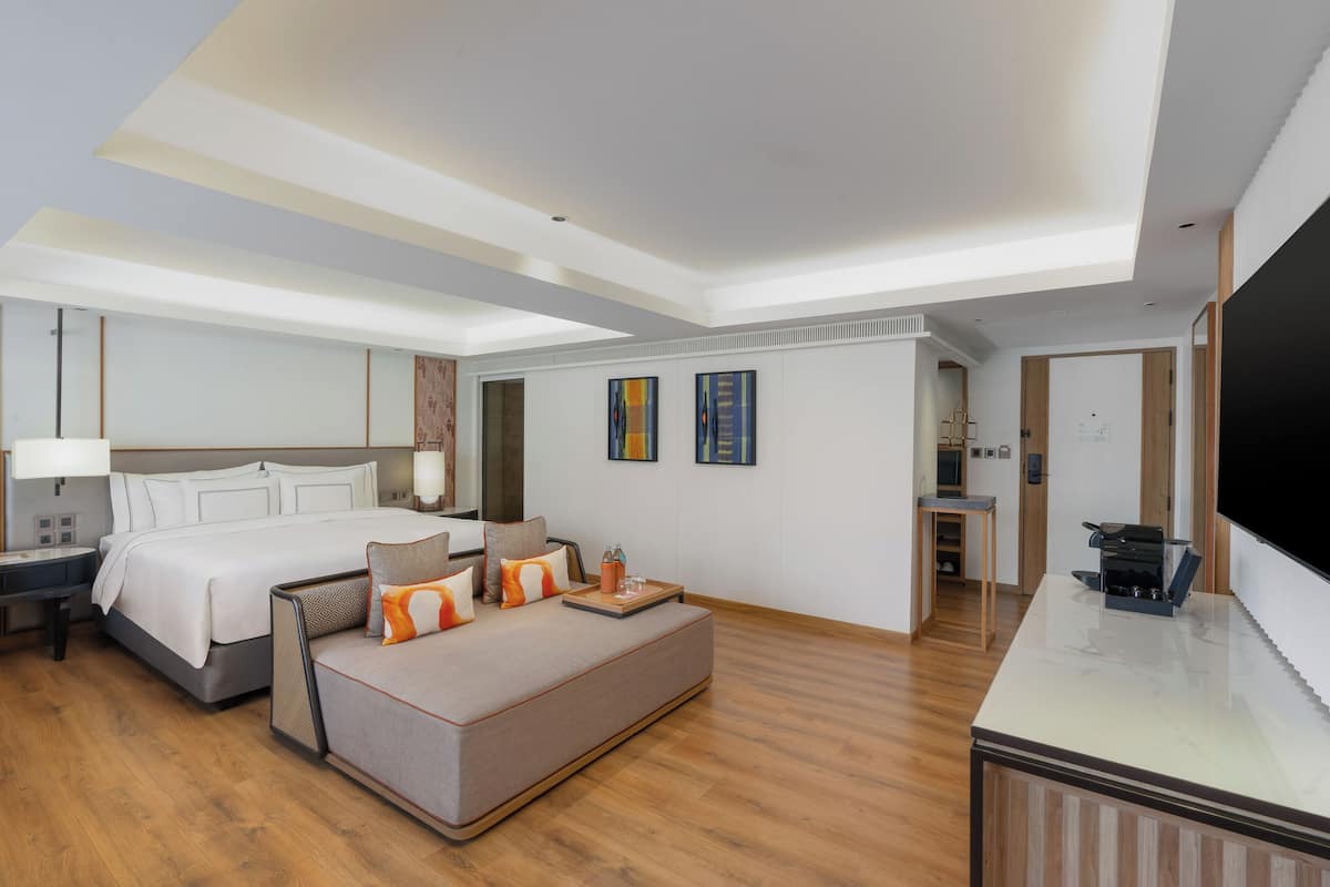 Ein modernes Hotelzimmer mit einem großen Bett, einer Sitzecke, einem Schreibtisch und einem Flachbildfernseher.