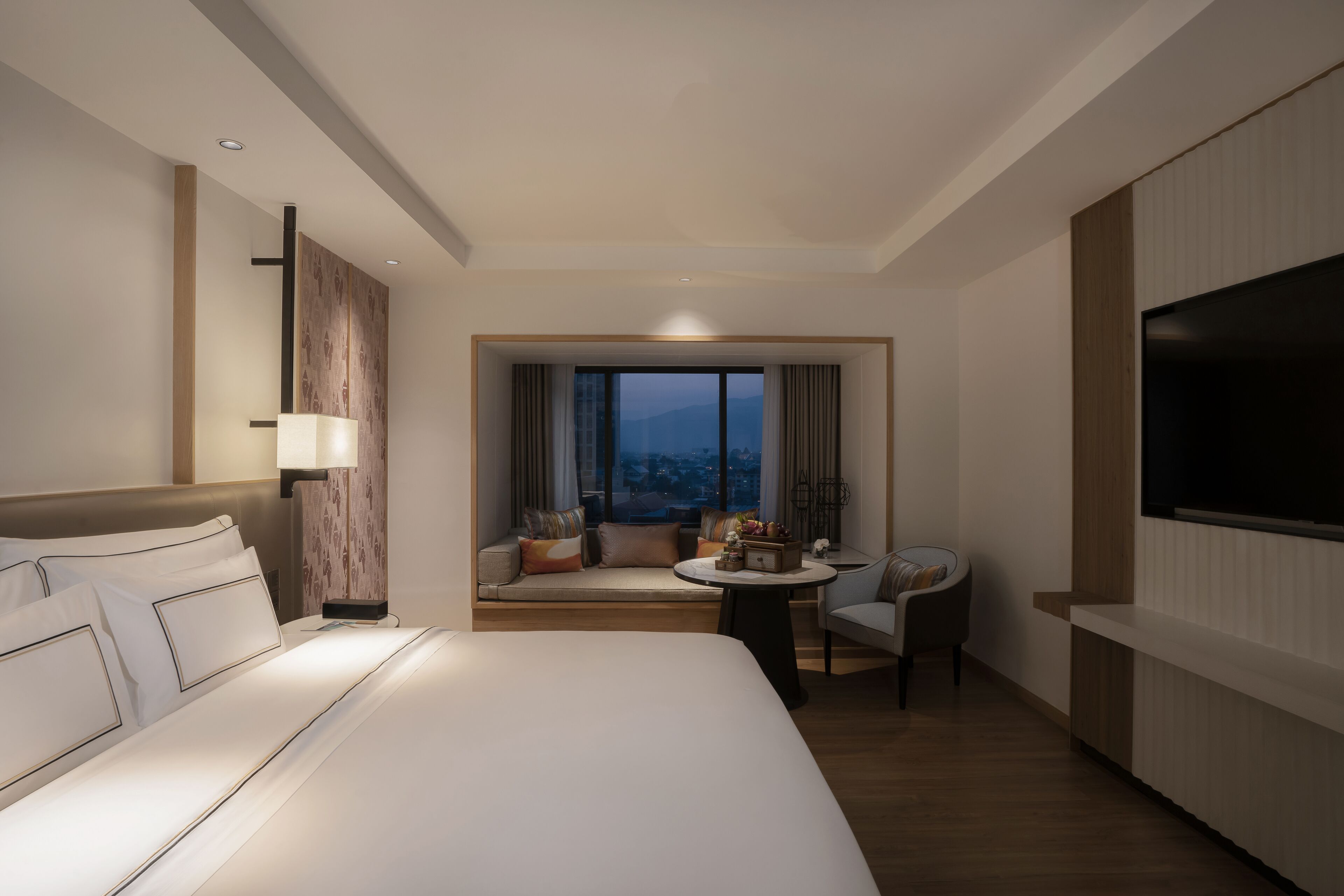 A hotel room with a large bed, a seating area with a view, a TV, and a desk.
