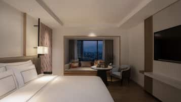 A hotel room with a large bed, a seating area with a view, a TV, and a desk.