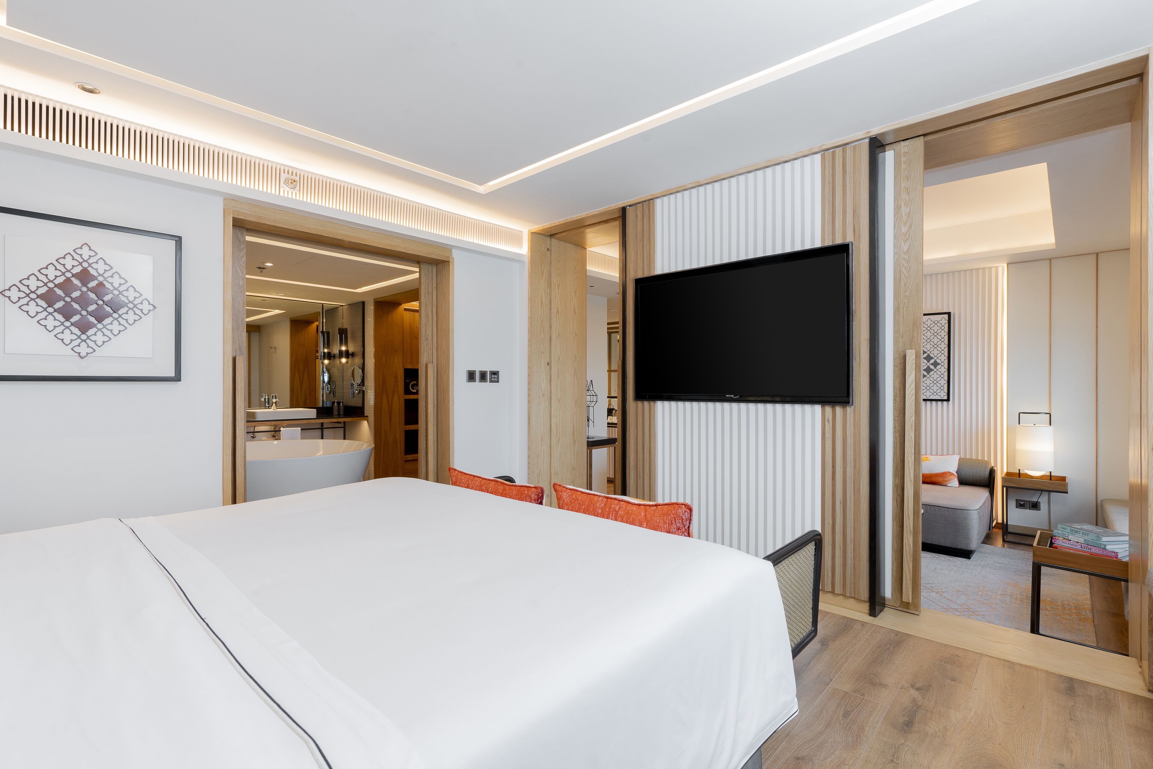 Una habitación de hotel moderna con una cama grande, un televisor de pantalla plana, un baño con espejo y una pequeña zona de estar con una mesa y una silla.