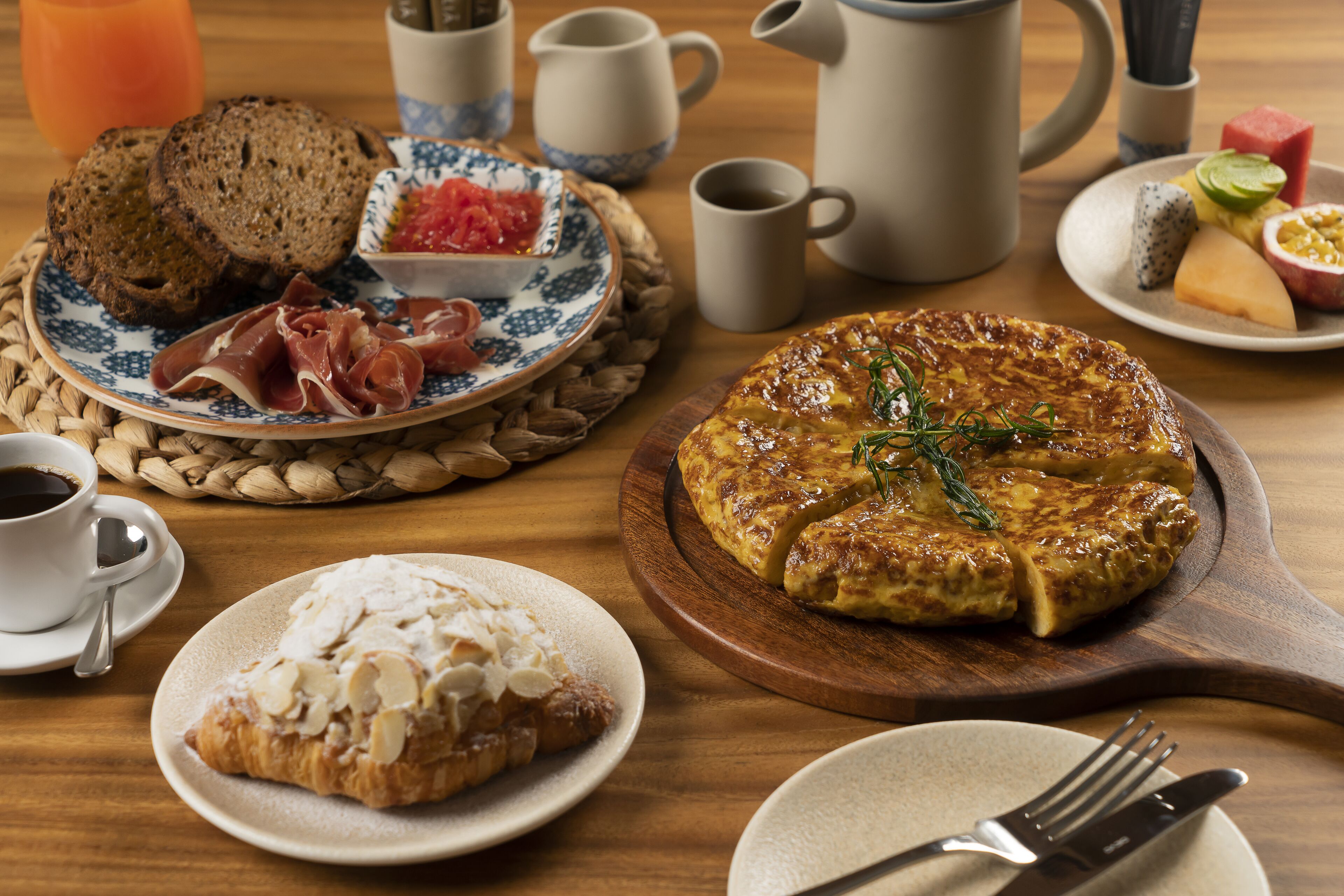 A breakfast setting with bread, pastries, and a variety of fruits and cheeses.