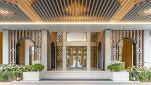 Une entrée d’hôtel moderne avec un plafond à lattes, de grandes portes cintrées et des plantes en pot.