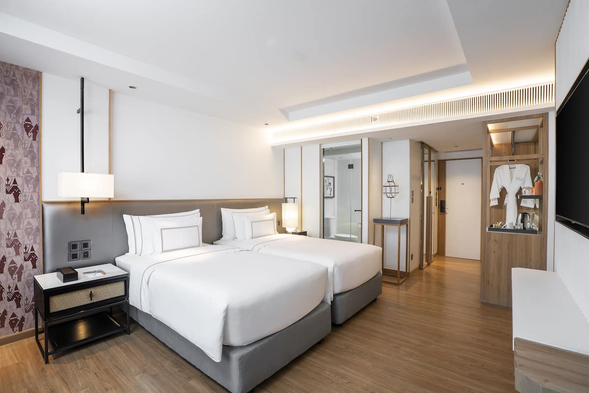 Ein modernes Hotelzimmer mit zwei Betten, einem Nachttisch, einer Lampe, einem Kleiderschrank und einem Spiegel.